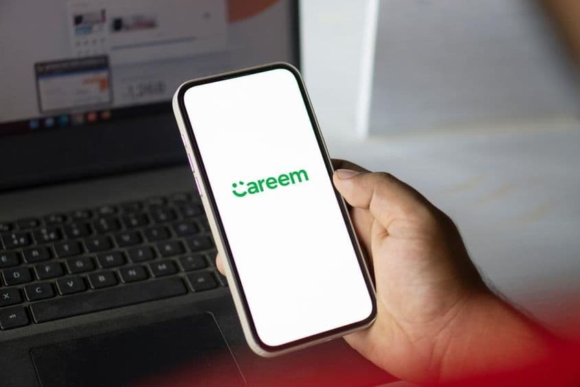手握着运行Careem应用的手机,背景中可见一本笔记本。
