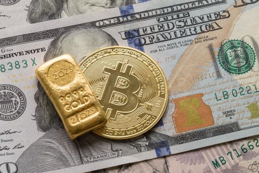 一根金条和一枚比特币硬币放在一张100美元纸币上。