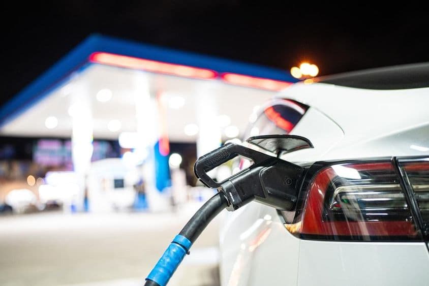 一辆特斯拉正在充电,背景是一个加油站。