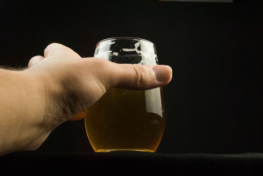 一只手握着一个啤酒杯,仅能看到手和杯子。
