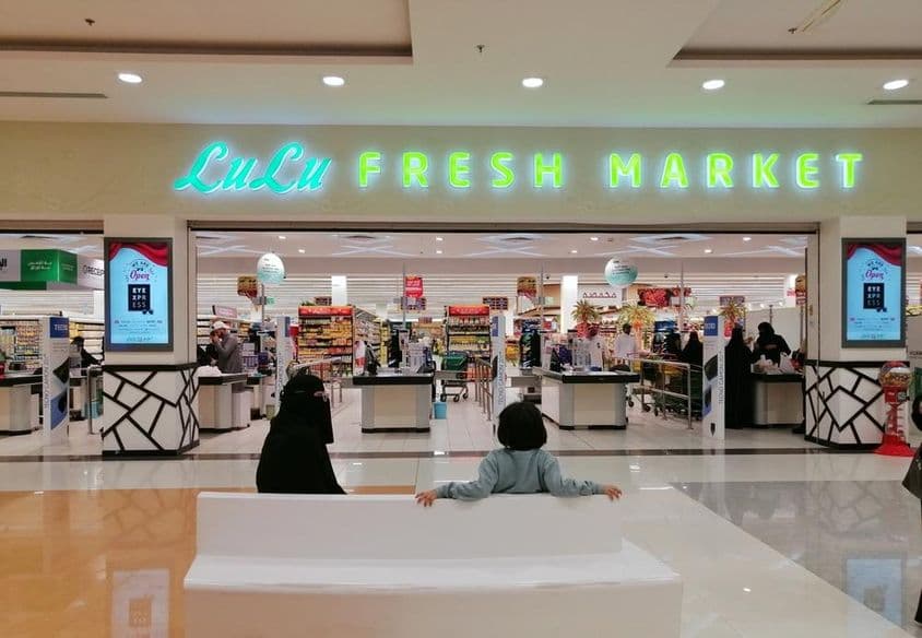 购物中心内的LuLu商店入口,看到一个女人和一个小孩坐在店门口,从后面看。