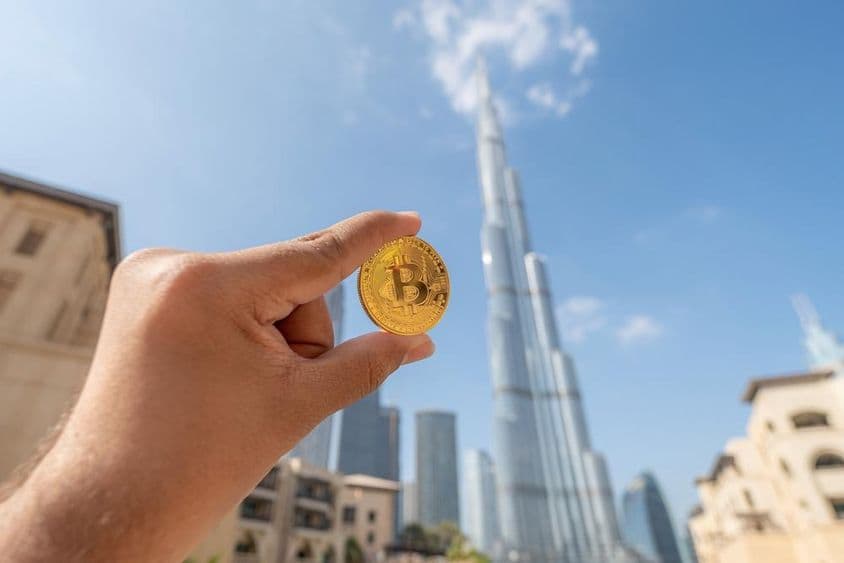 一个人手持金色比特币硬币,面向天空,背景是迪拜哈利法塔。