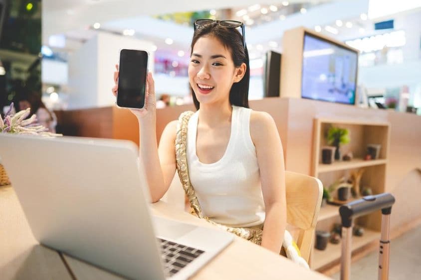 Z世代女孩工作,握着手机,前面放着笔记本,旁边有行李箱把手。