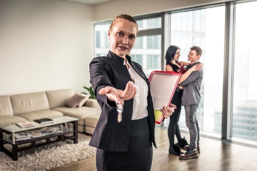 一位女性地产经纪人挥手,背景中一对情侣正在拥抱。