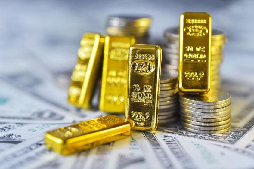 999.9纯金投资金条静卧在美元钞票上,旁边有金属硬币。