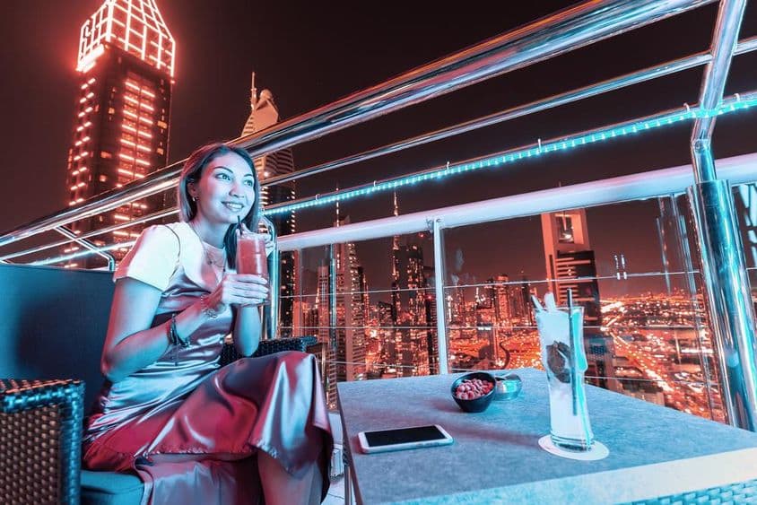 年轻女子在迪拜屋顶酒吧露台喝鸡尾酒。