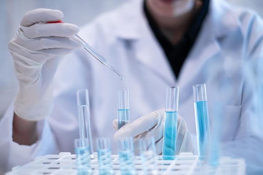 科学家正在实验室中用移液管吸取蓝色液体到试管中。