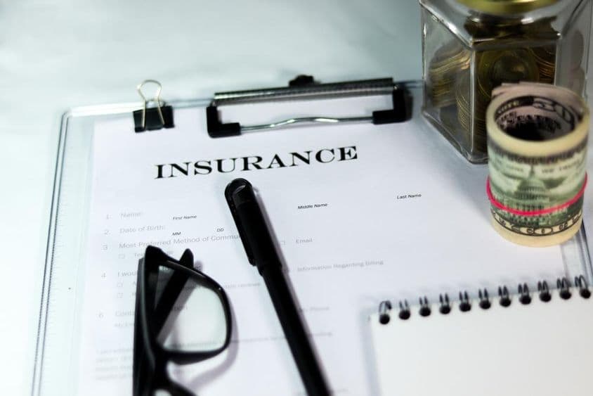 保险表格与硬币盒子、美元捆、笔和眼镜