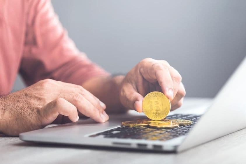 一名男子手持金色比特币并使用笔记本电脑。