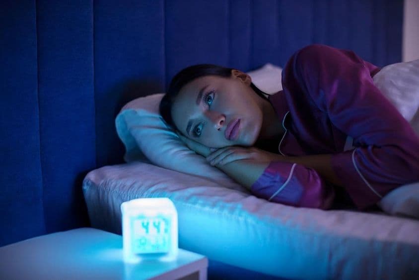 失眠女士躺在床上,无法入睡,凝望远处,表情忧伤。