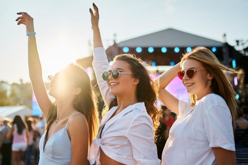 身穿夏装的女孩们享受音乐会,欢庆时举起双手。