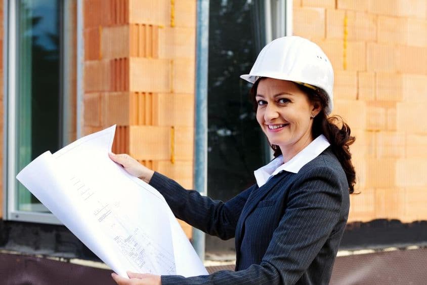 头戴安全帽的女性建筑师手持蓝图站在建设中的房屋前