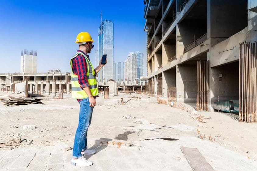 在迪拜建筑工地背景下使用智能手机的男子,城市天际线作为背景。