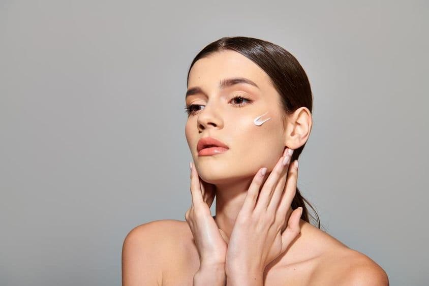 一位棕发年轻女性在脸上涂抹美容霜,散发出一种自我护理的感觉。