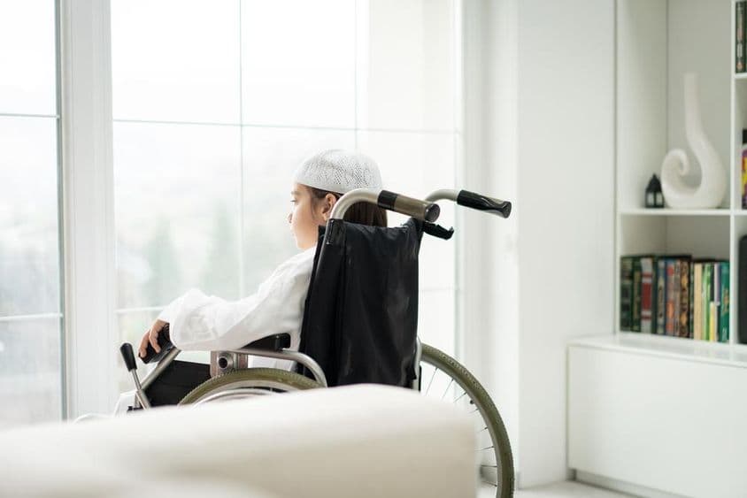 坐在轮椅上的年轻男孩透过窗户看