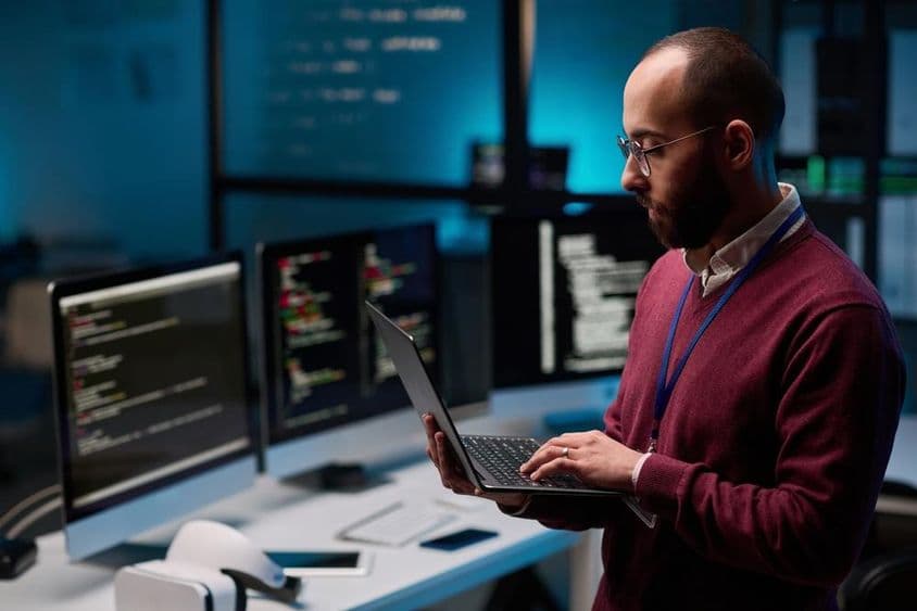 在IT和网络安全办公室中,一名电脑程序员拿着一台打开的笔记本电脑。