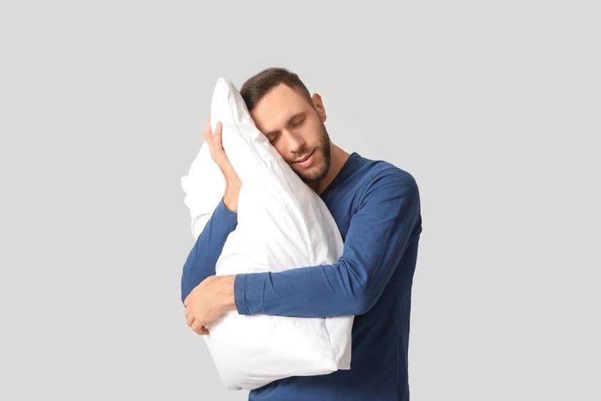 穿着睡衣,抱着柔软枕头的年轻男子。