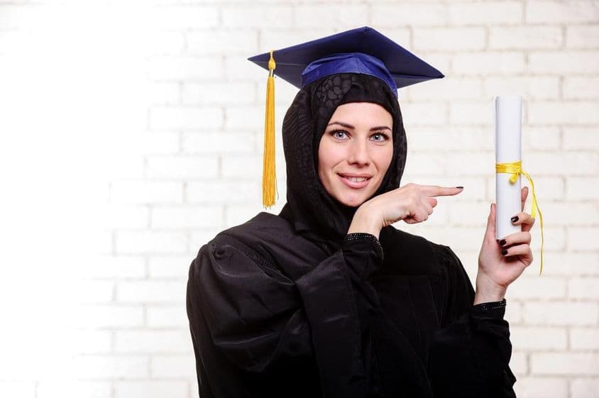 穆斯林毕业生在室内持毕业文凭开心拍照。