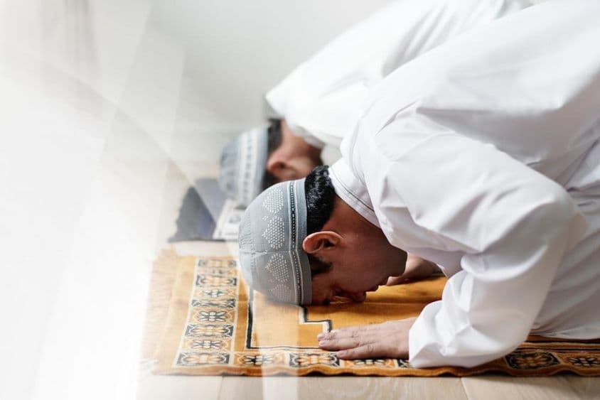 身穿白色礼服的伊斯兰男子在祈祷中鞠躬。