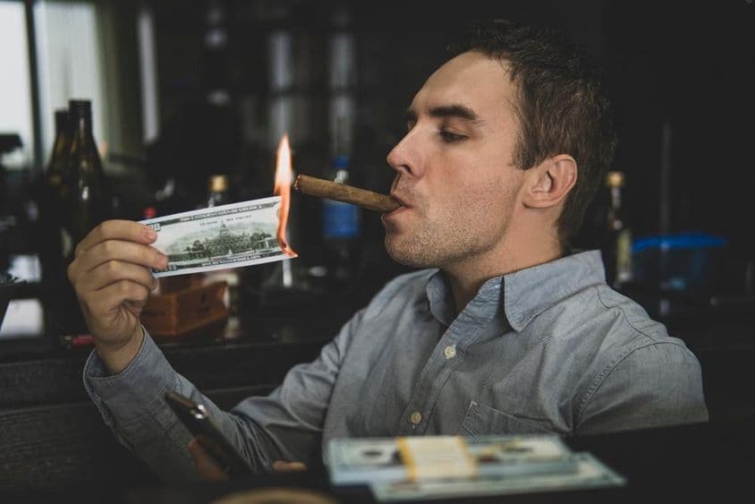 年轻帅气的男人在酒吧用百元美钞点燃雪茄。