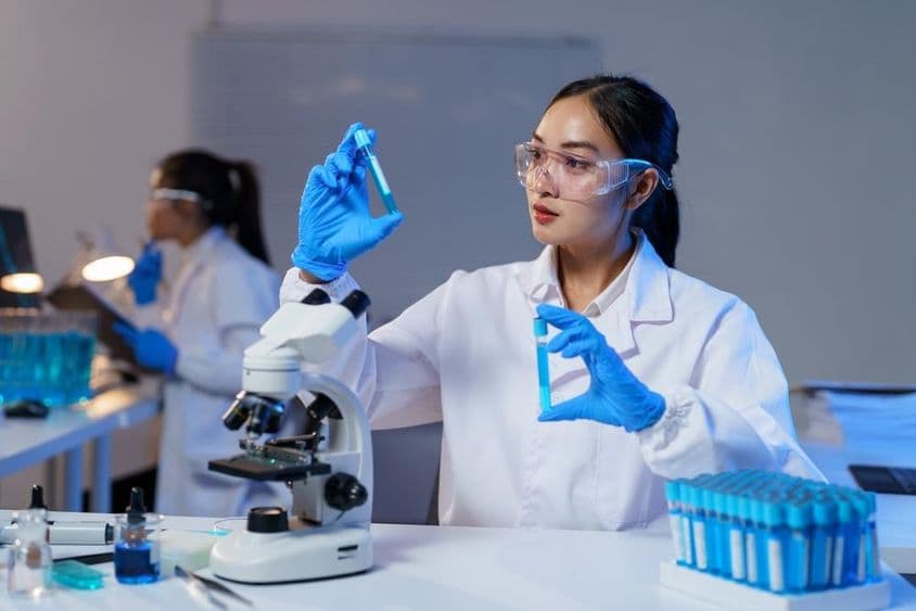 穿着实验室外套和手套的亚洲女性科学家比较两个试管