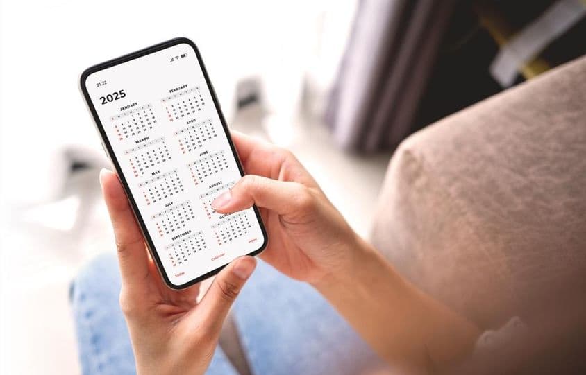 职场女性用智能手机和月历规划2025年活动。