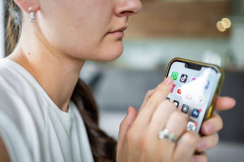 一位女性手持iPhone,屏幕上显示着WhatsApp聊天应用。