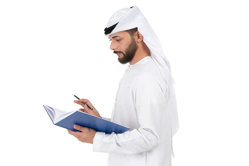 年轻的阿拉伯教师站着在书上写字。