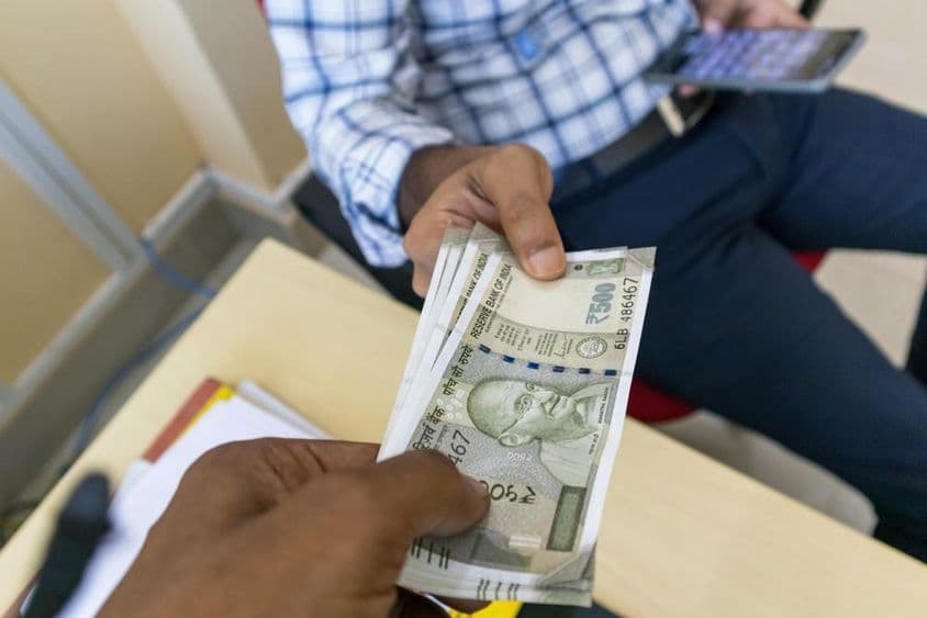 一个人将500卢比的印度钞票递给另一个人。