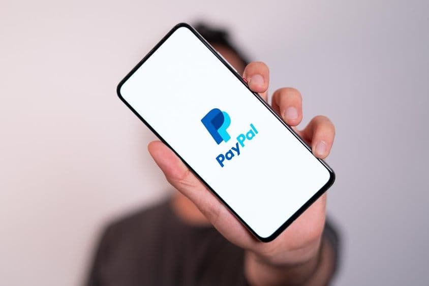 一个人拿着手机,手机屏幕上可见PayPal标志。