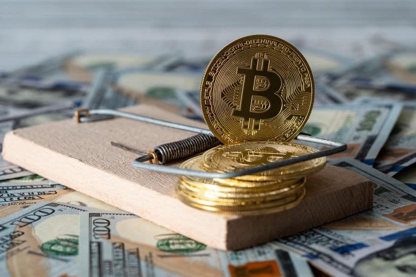 金色加密货币比特币在捕鼠器中,背景是100美元纸钞。