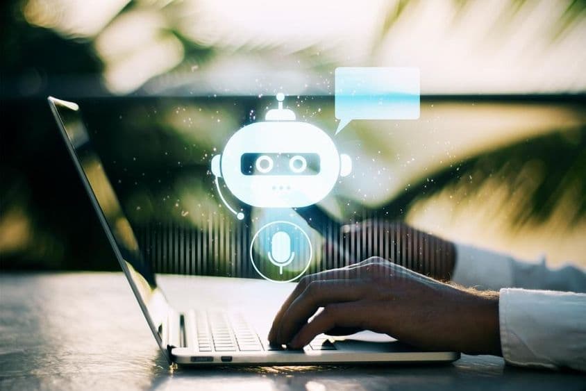 一个人正在户外背景模糊的情况下在笔记本电脑上打字,旁边有一个聊天机器人图标。